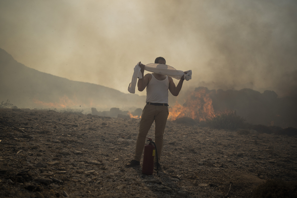 A man wraps his shirt over his face as he tries to extinguish a fire.